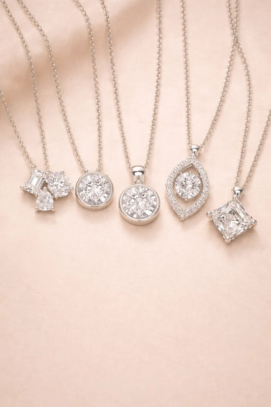 Five elegant silver solitaire diamond necklaces with various cut stones on a soft beige background.
