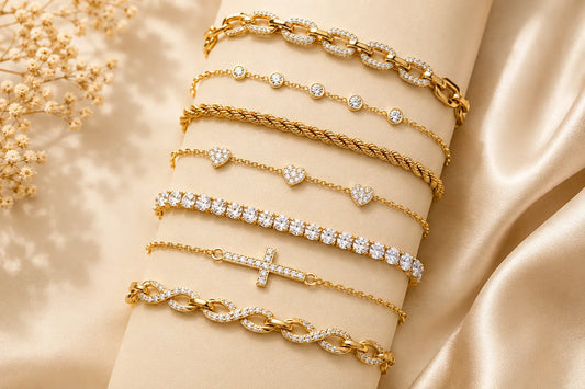 Seven elegant gold bracelets featuring diamonds, heart charms, and a cross on a beige satin background.
