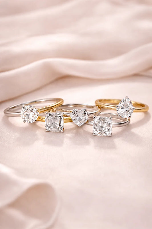 Five elegant solitaire engagement rings with varied diamond cuts on a soft, draped silk background.