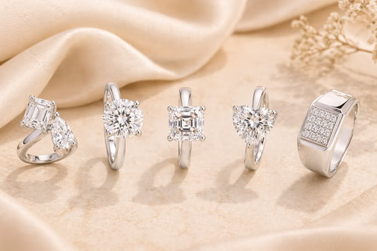 Five elegant silver rings featuring diverse diamond cuts, including heart, round, and emerald shapes, on satin fabric.